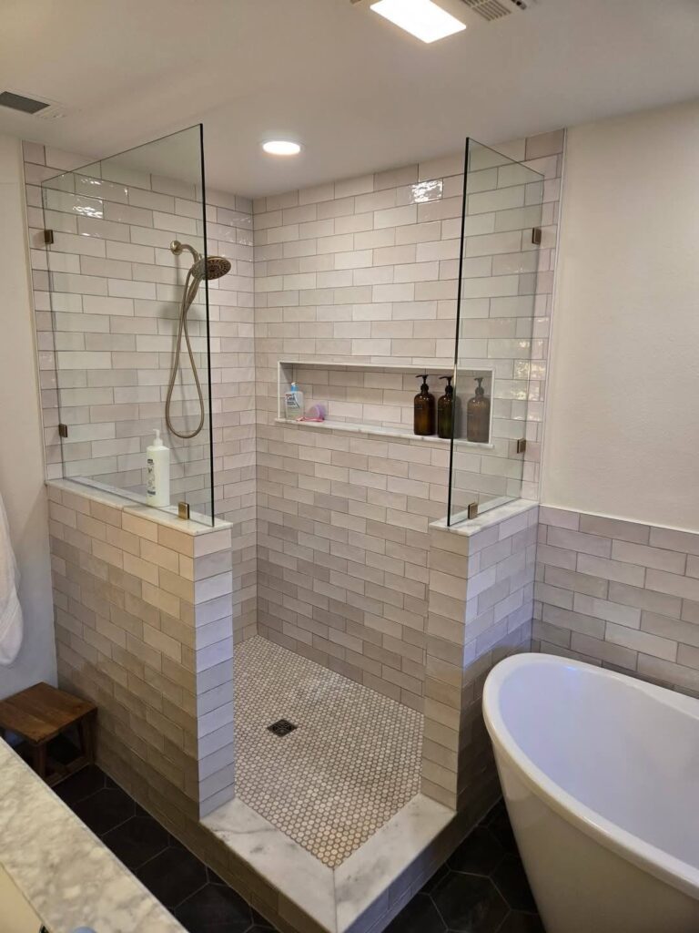 Walk-in shower tile installation with glass enclosure and built-in niche