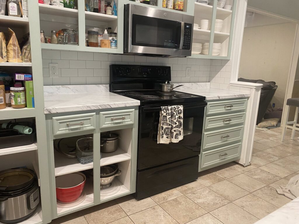 Kitchen floor tile installation with white cabinets and black appliances by JPond Custom Tile